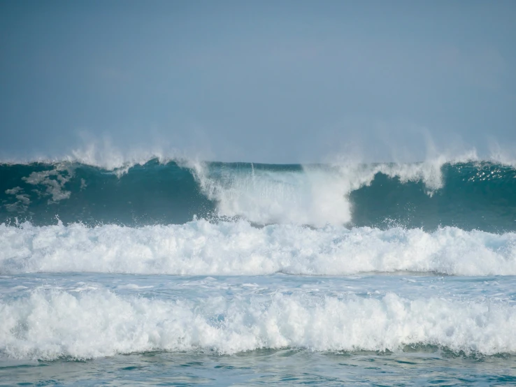 three waves are rolling over the shoreline and one man stands on the edge