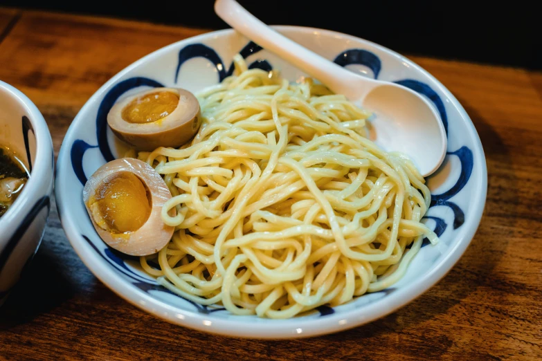 a bowl with noodles and an egg sits next to a bowl with two eggs