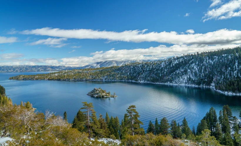 an evergreen covered hill with some trees on the sides and large body of water at the end