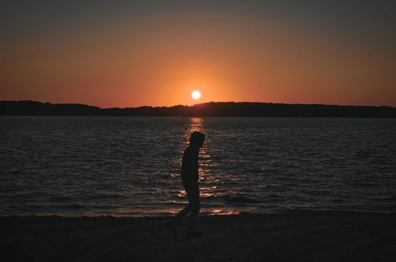 person standing in the middle of the water watching the sun set