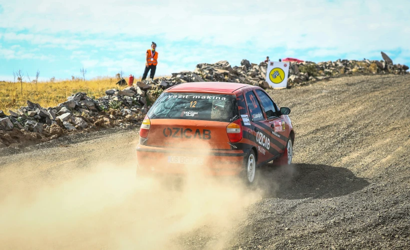 man driving a red car on dirt track near a rock wall