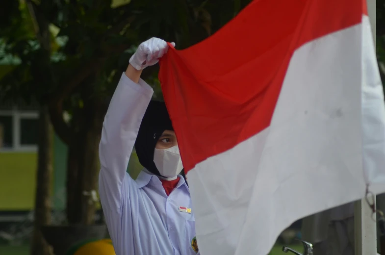 the young person in the white jacket is covering his face with a red and white flag