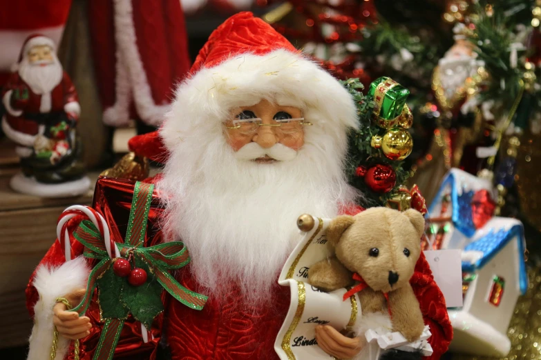 a santa claus figure holding a teddy bear near a christmas tree