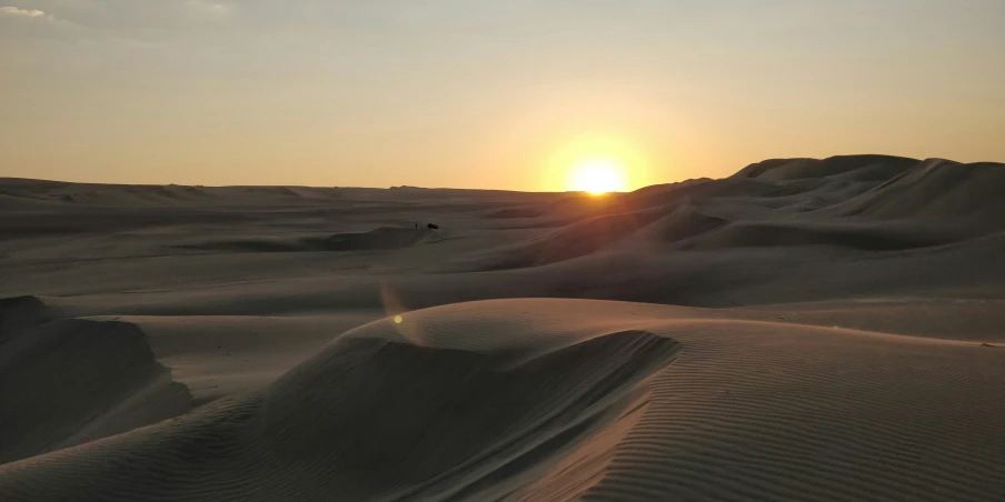 the sun is setting behind the sandy mountains