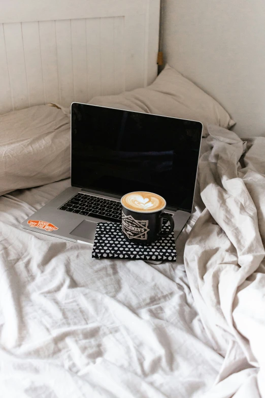 a laptop and coffee cup on a white bed