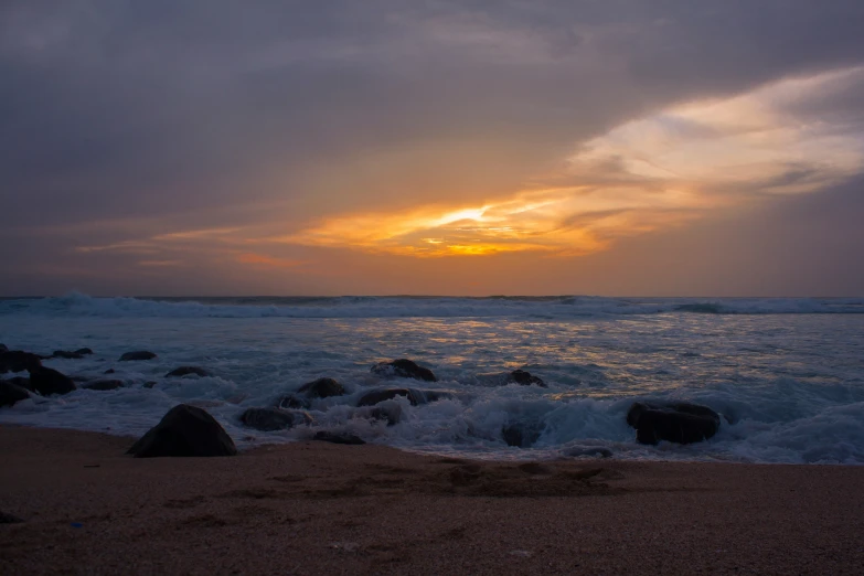 the sun sets over the ocean, and some rocks are in front