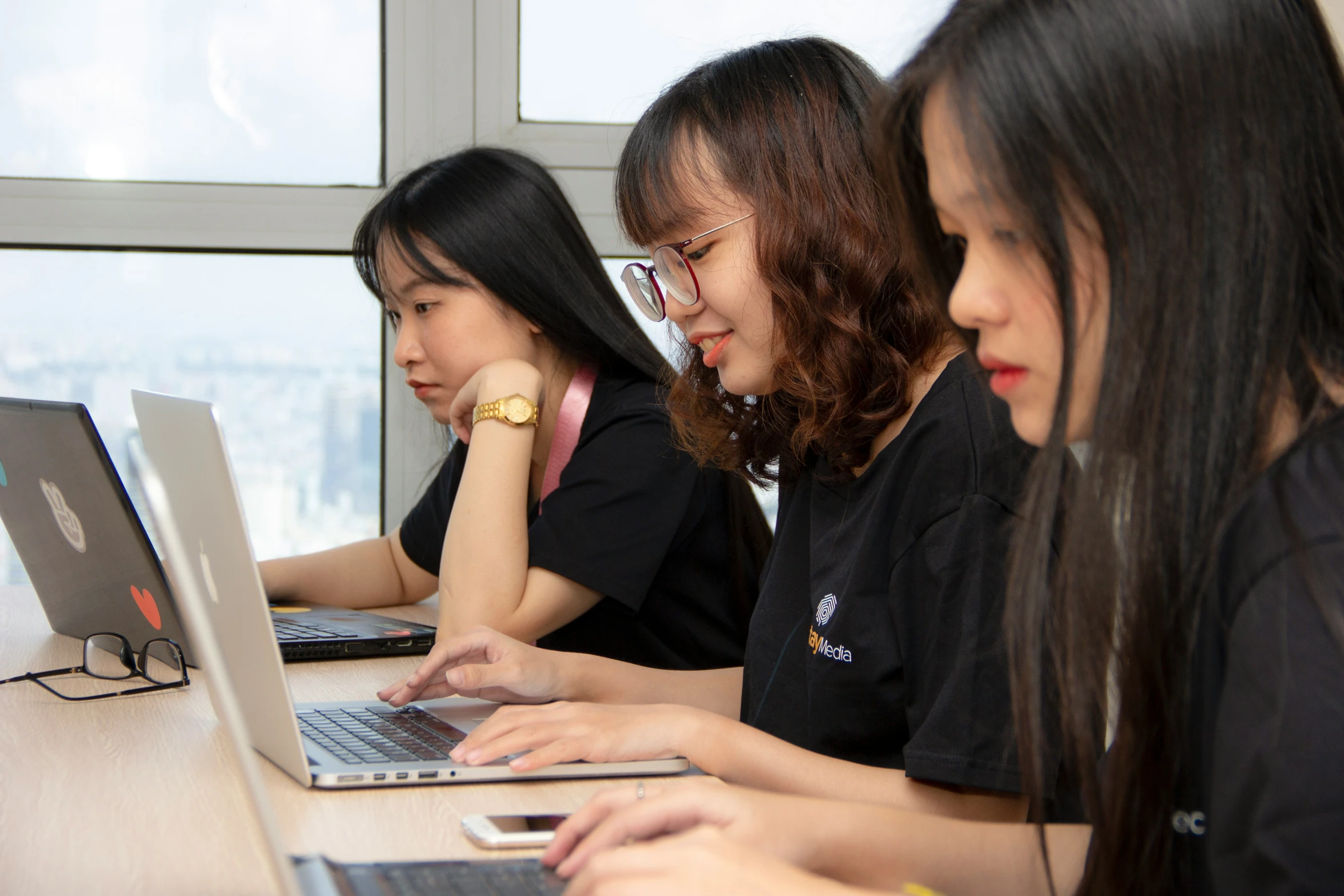 four asian students sit at their laptop computers