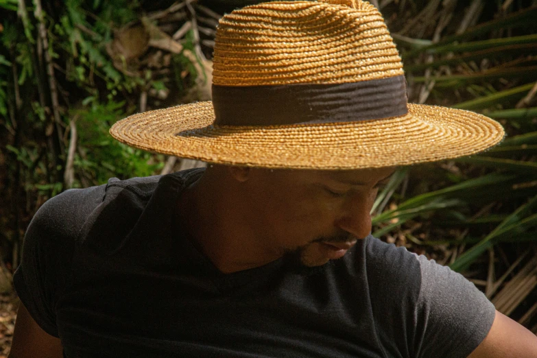 a man wearing a straw hat sitting in front of a jungle
