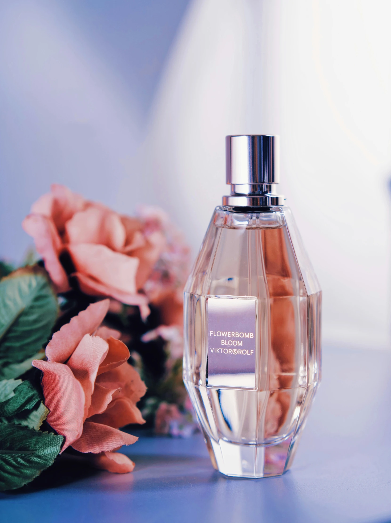 a small bottle of perfume next to some pink flowers