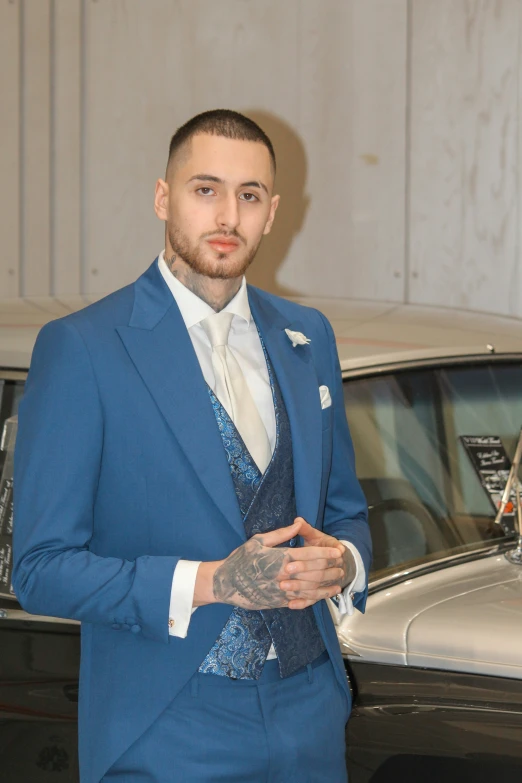 a tattooed man wearing a suit stands in front of a black car