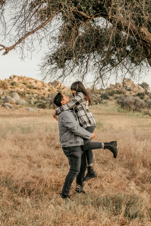 a couple hugging under a tree as the woman lifts her husband