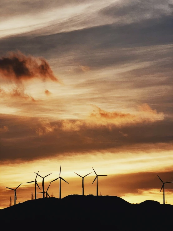 a group of wind mills on a hill with some clouds