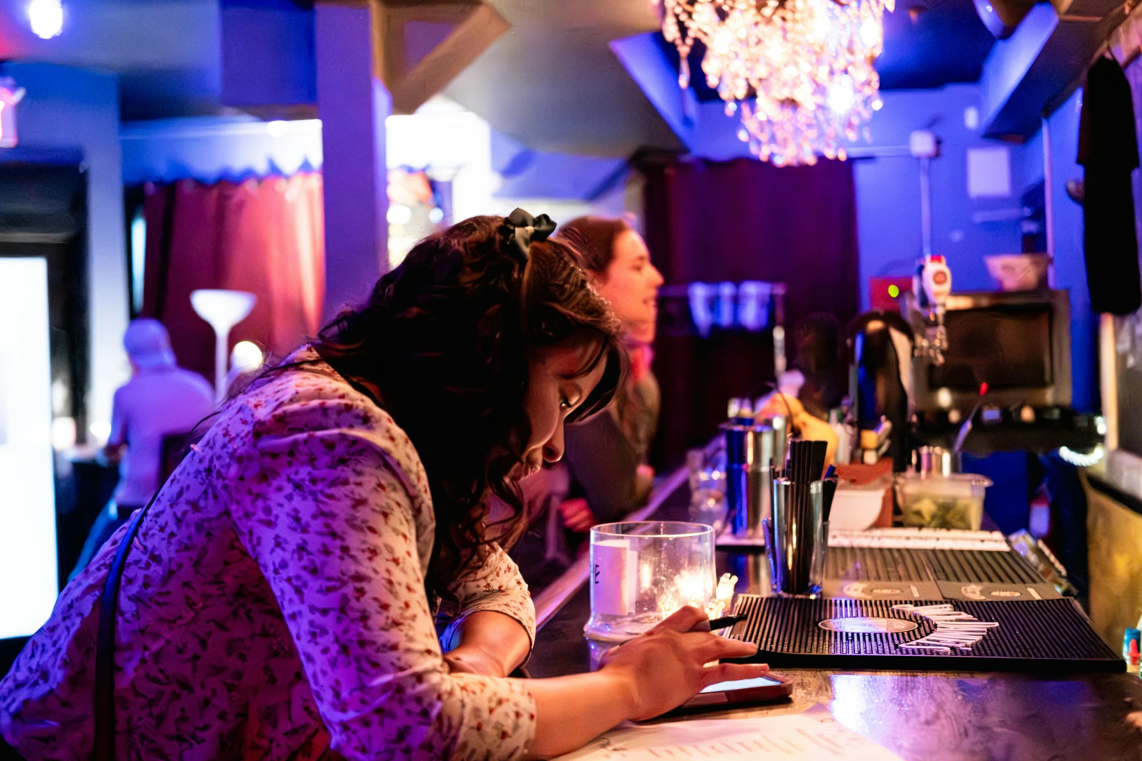 a woman looks at her phone and smiles as she stands at the bar