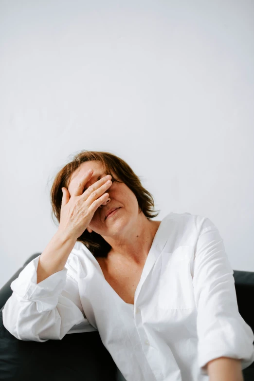 a woman covering her eyes while sitting on a chair