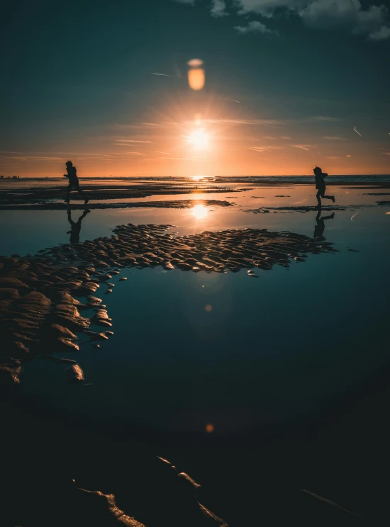 the people are walking on the beach at sunset