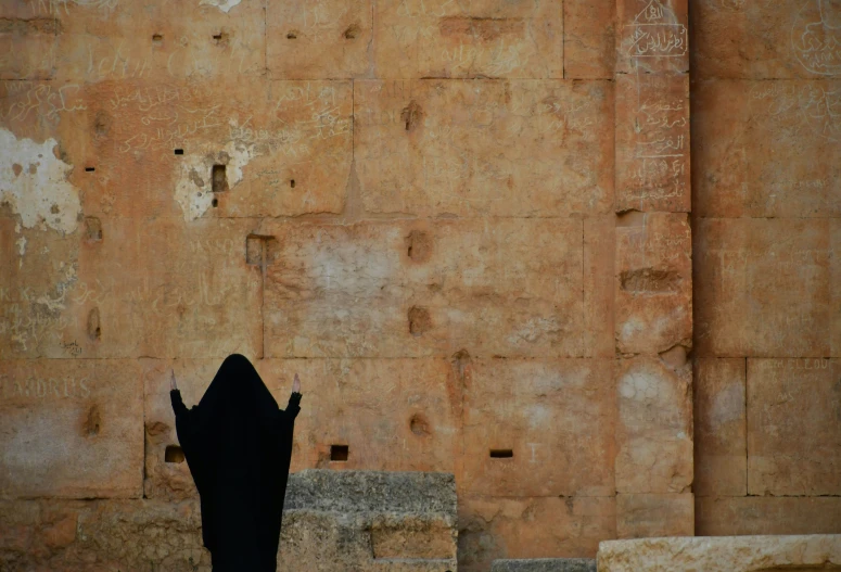 silhouetted woman standing near old wall with graffiti