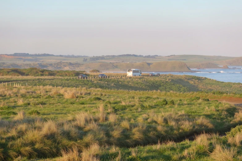 several vehicles driving down a grassy hill next to the ocean