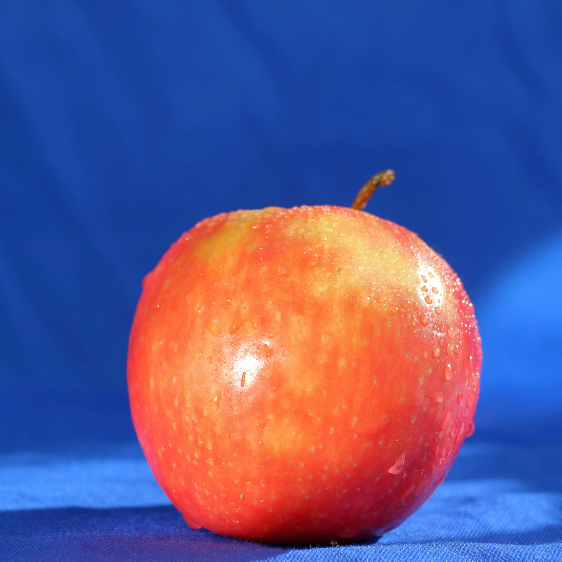 an orange colored apple on a blue table cloth