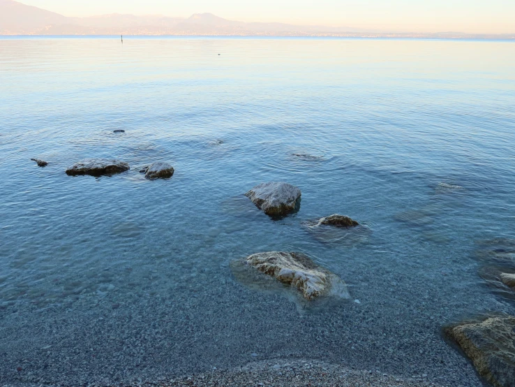 clear blue water has rocky banks of beach, rocks and sky