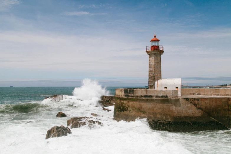 a lighthouse that is perched on a cliff with waves crashing near it