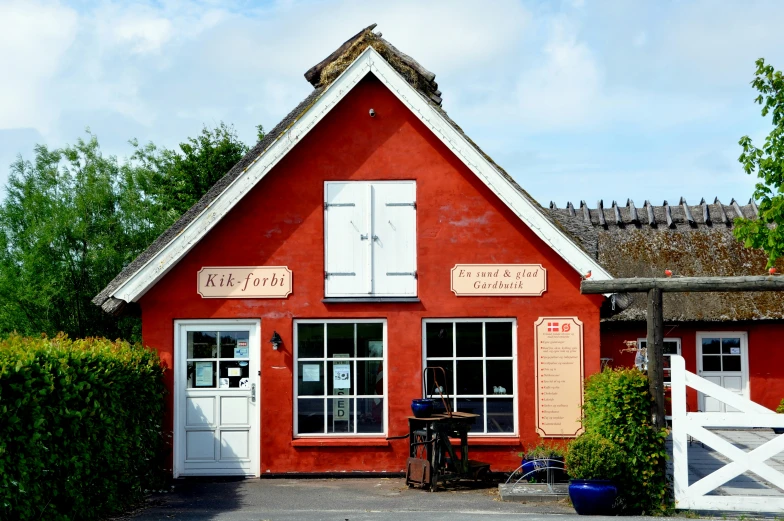 an old red building with white shutters and two tall plants