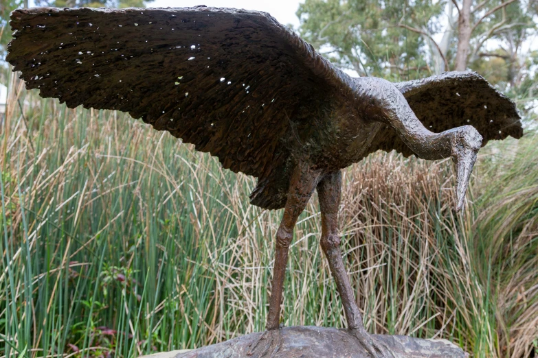 a bird statue in the grass next to some tall plants