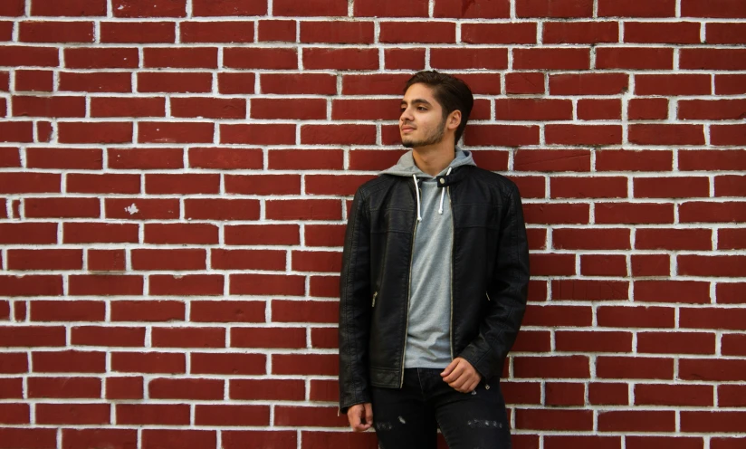 a man is standing against a red brick wall