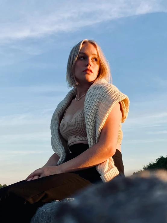 a woman is sitting on a rock against the sky