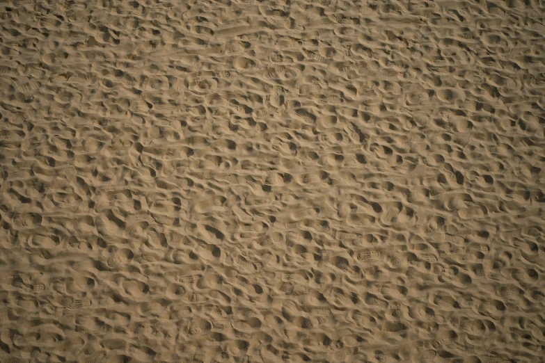 a brown sandy beach with footprints and a brown chair