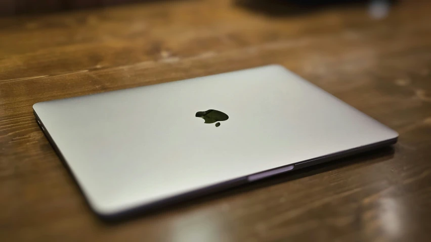 an apple laptop sits on a wooden table