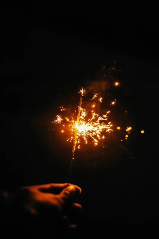 someone holding a lit sparkler with a black background