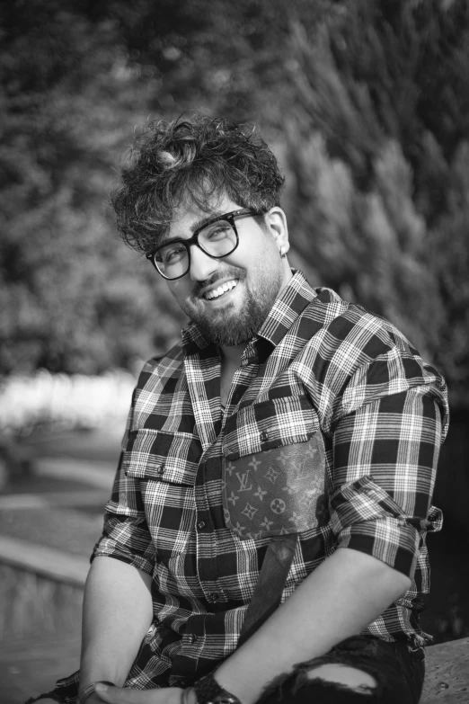 a man sitting in front of a bunch of trees wearing glasses