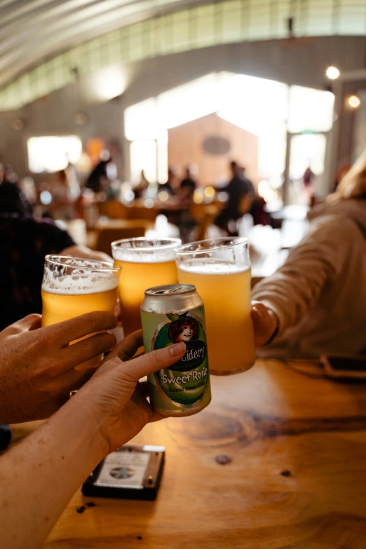 people are holding beers in their hands as they sit at a table with cell phones