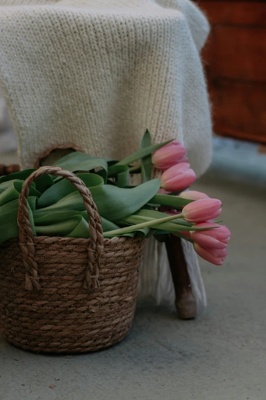 pink tulips and green leaves in wicker basket on table