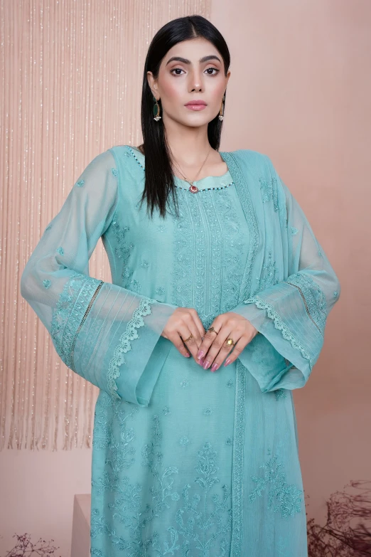 a woman with dark hair wearing a light blue dress and standing in front of a wall