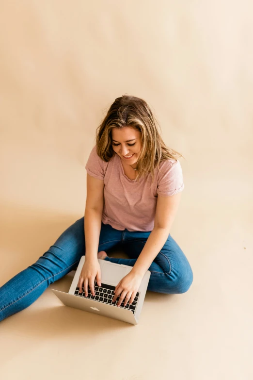 a young woman sits on the ground and plays with a laptop