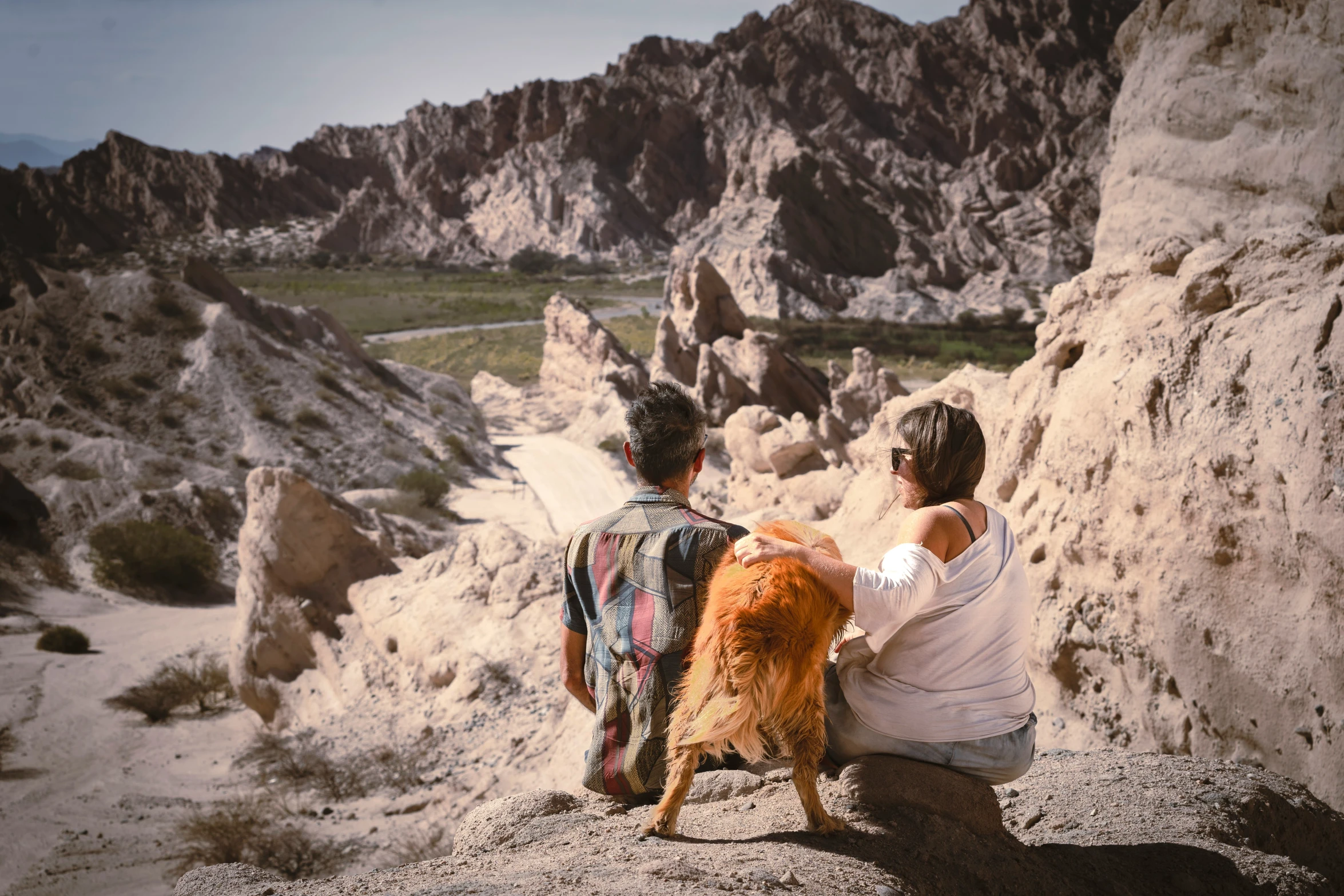 two boys and their dog are sitting on the rocks in the desert