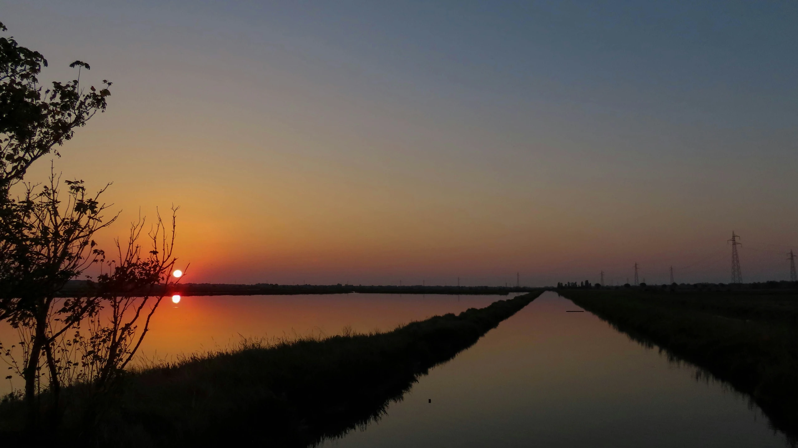 the sun sets behind trees and water along the edge of a waterway