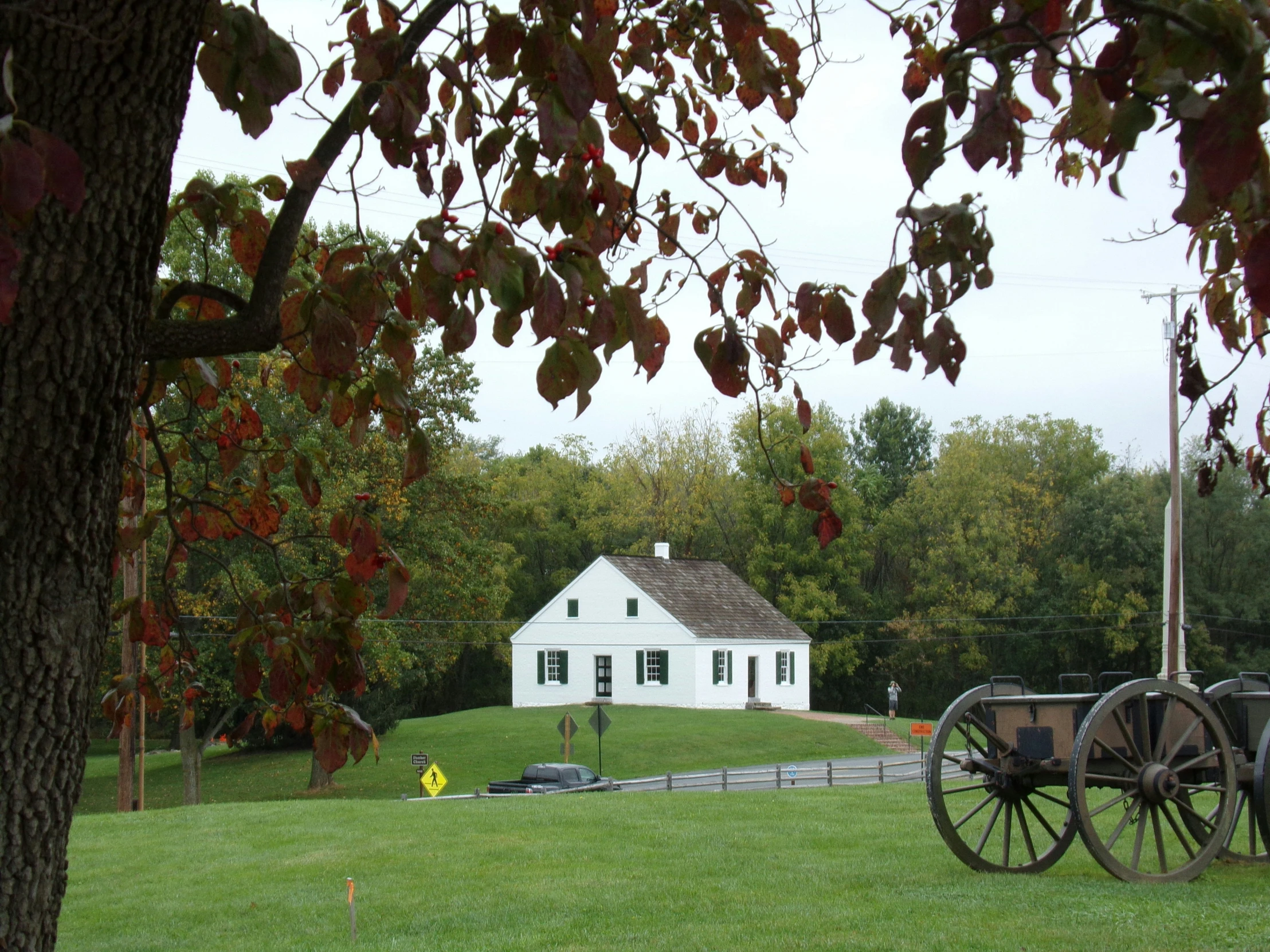 a old fashioned wagon and white house are sitting behind a tree