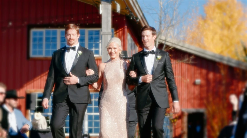 three people walking in front of a red barn