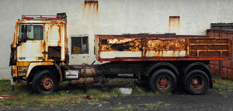 the rusted out truck sits outside of a dilapidated building