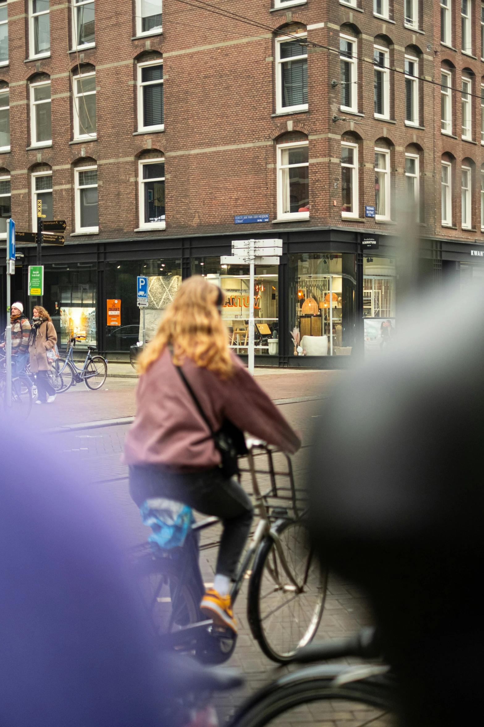 a large brick building behind a tall person riding a bike down the street