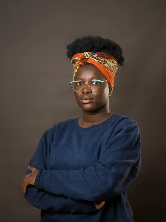 a woman standing with her arms folded, wearing glasses and a turban