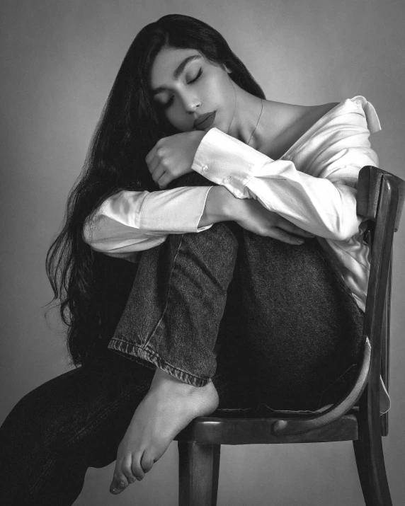 a woman wearing a shirt and jeans, sitting on a wooden chair