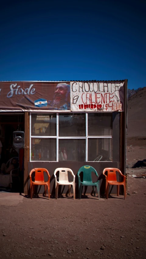 three different colored chairs are standing outside a restaurant