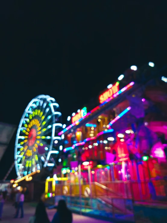 people walking near a brightly lit building and ferris wheel at night