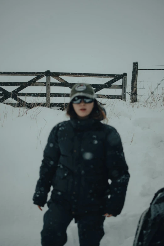 a person stands in the snow near a fence