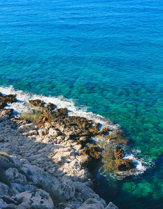 a sea side view of clear blue water and rocky shoreline