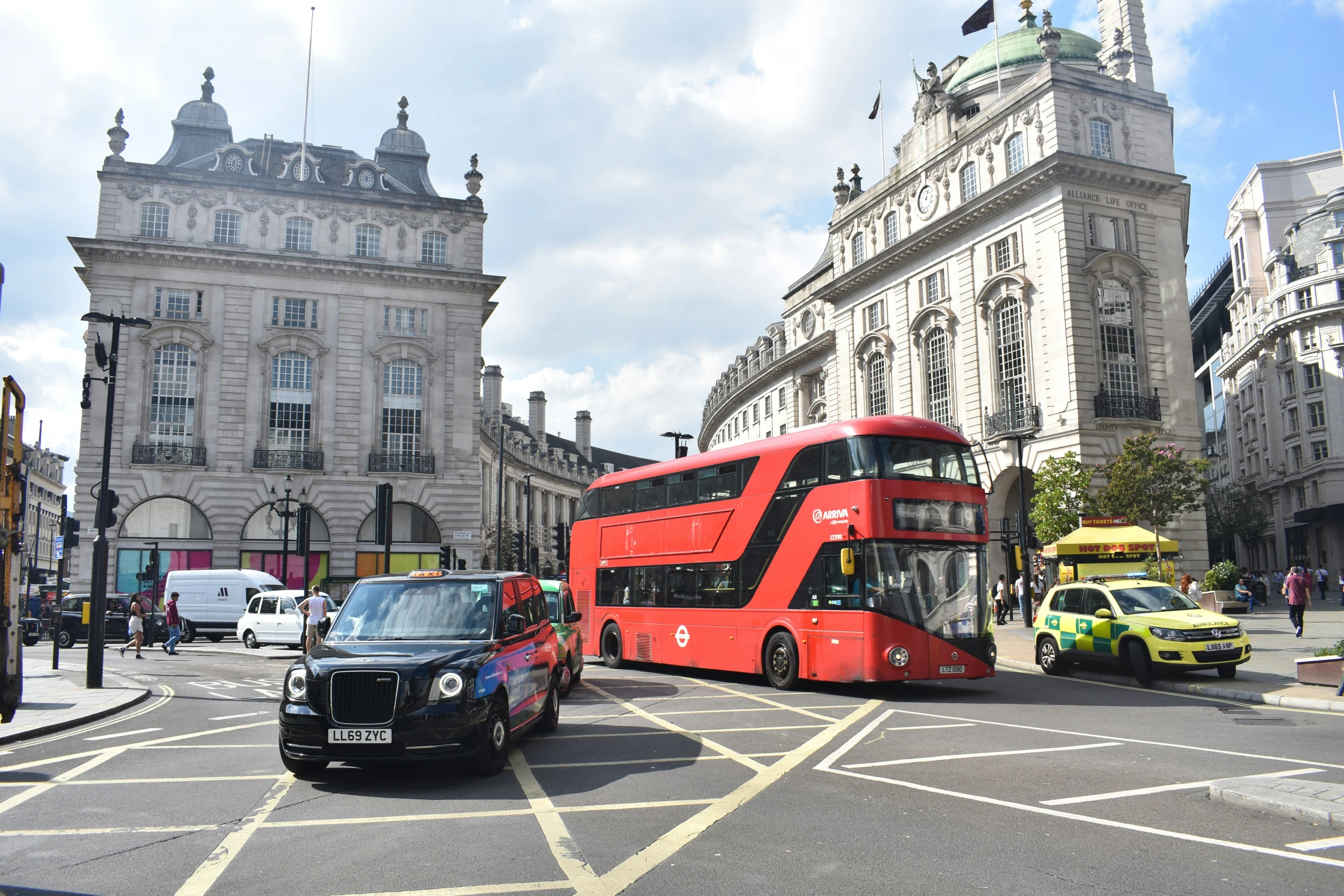 a red double decker bus driving down a street next to tall buildings