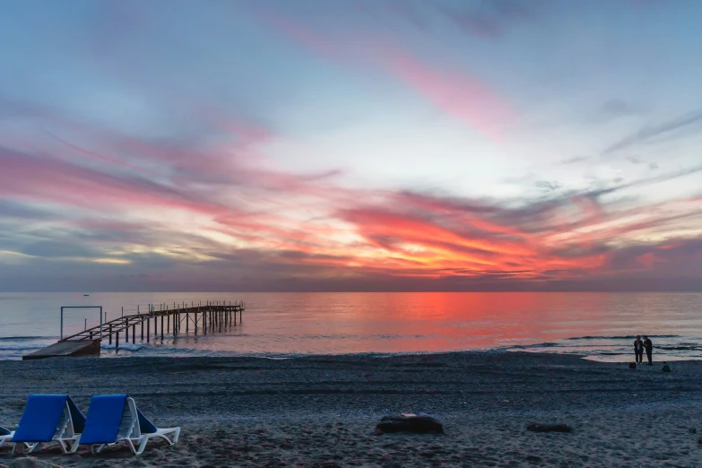 people on the beach at sunset with the sky painted in pink